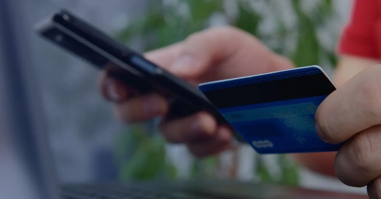 Zoomed-in picture of a man's hand holding a credit card and a phone about to buy something